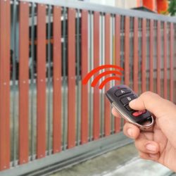 Female hand holding and showing remote control to open or close the automatic wooden gate with home blurred background. Security and save time concept.